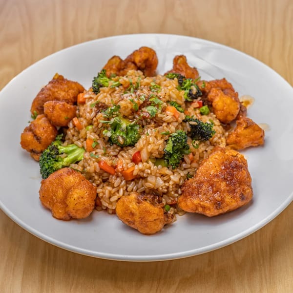 Vegan fried rice with broccoli, carrots, and crispy orange cauliflower on a white plate.