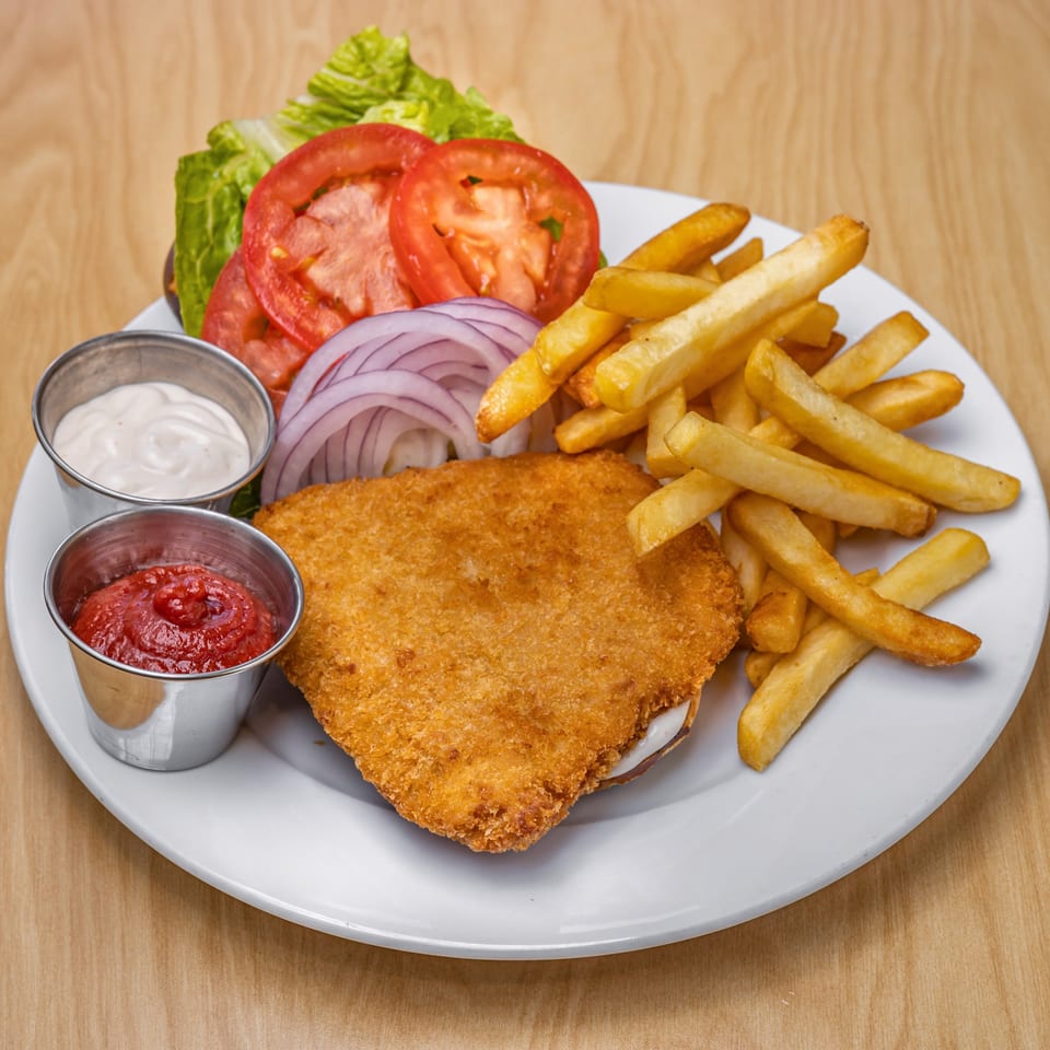 Vegan fried chicken sandwich with lettuce, tomato, onion, fries, ketchup, and mayo on a white plate.