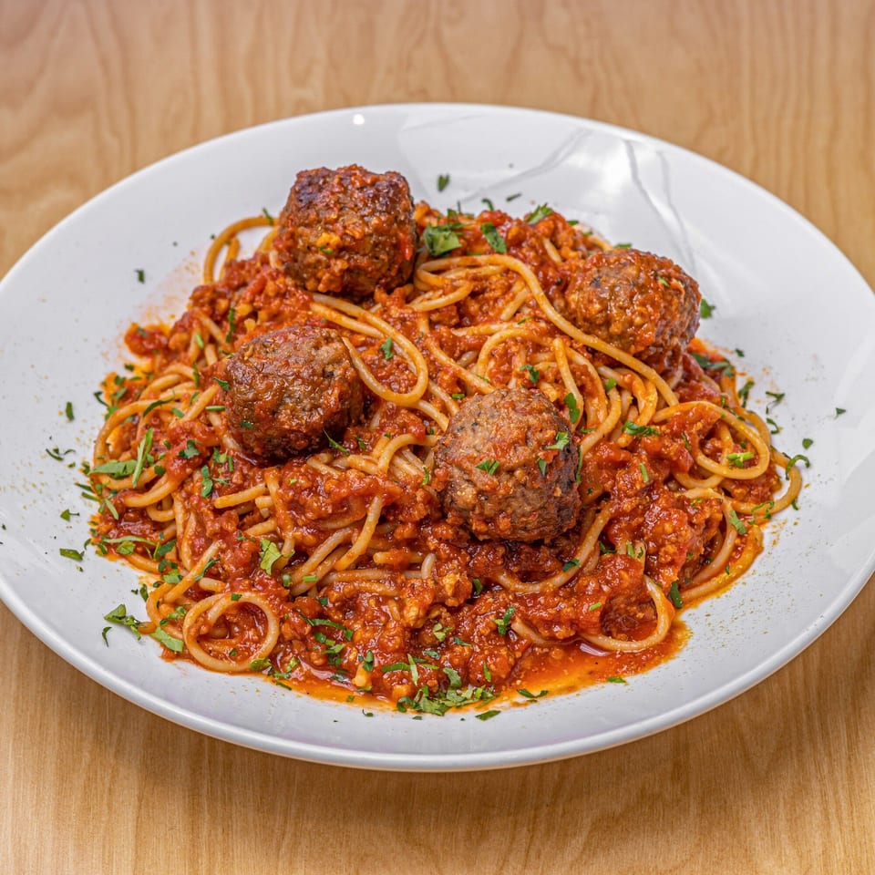 Vegan spaghetti and meatballs with rich red sauce and fresh parsley on a white plate.