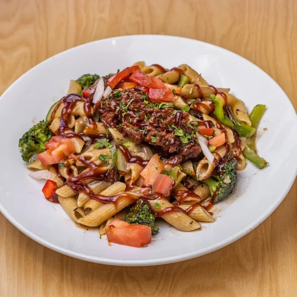 Vegan penne pasta with broccoli, tomatoes, peppers, and a rich brown sauce on a white plate.