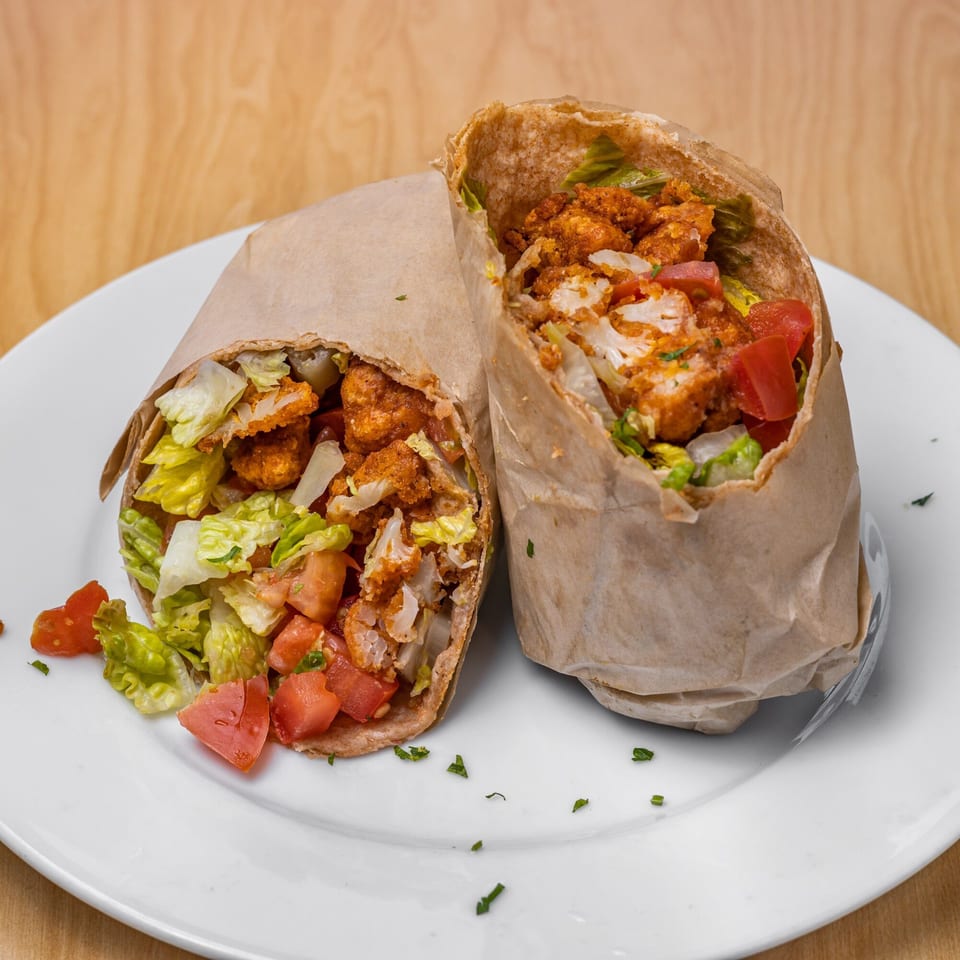 Two vegan wraps, filled with crispy cauliflower, lettuce, and diced tomatoes, on a white plate.